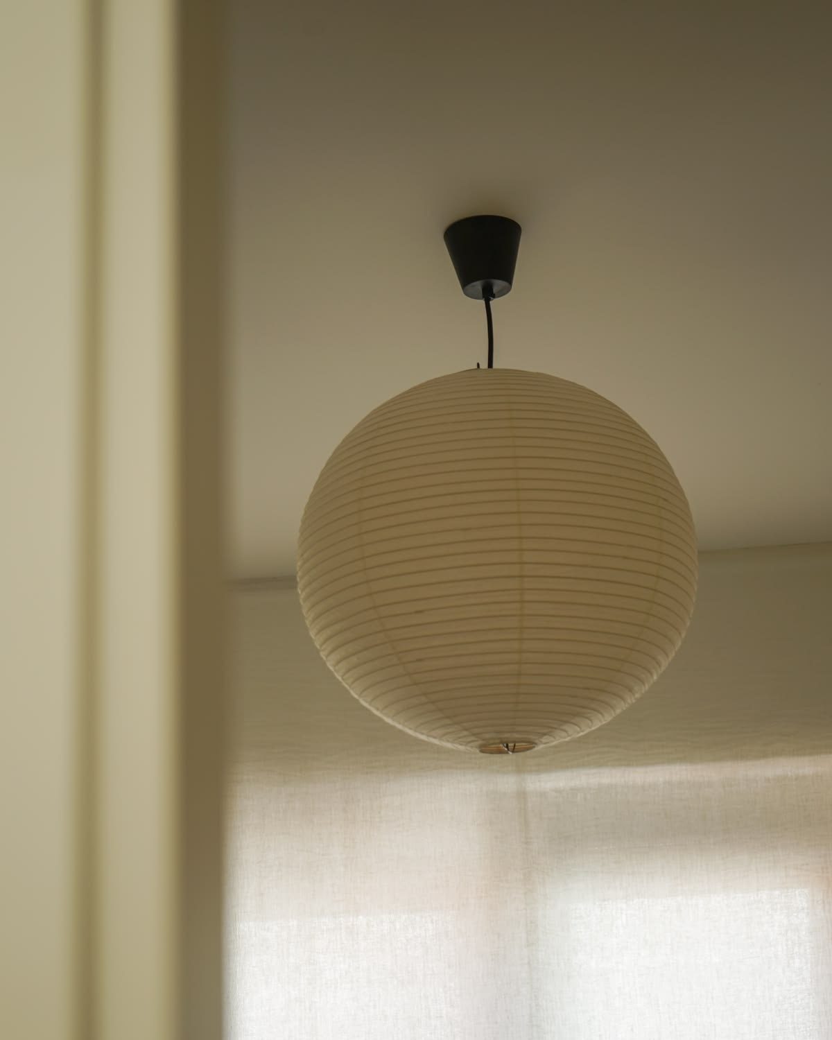 Close view of the AKARI 30A shade hanging in front of a sunlit curtained window